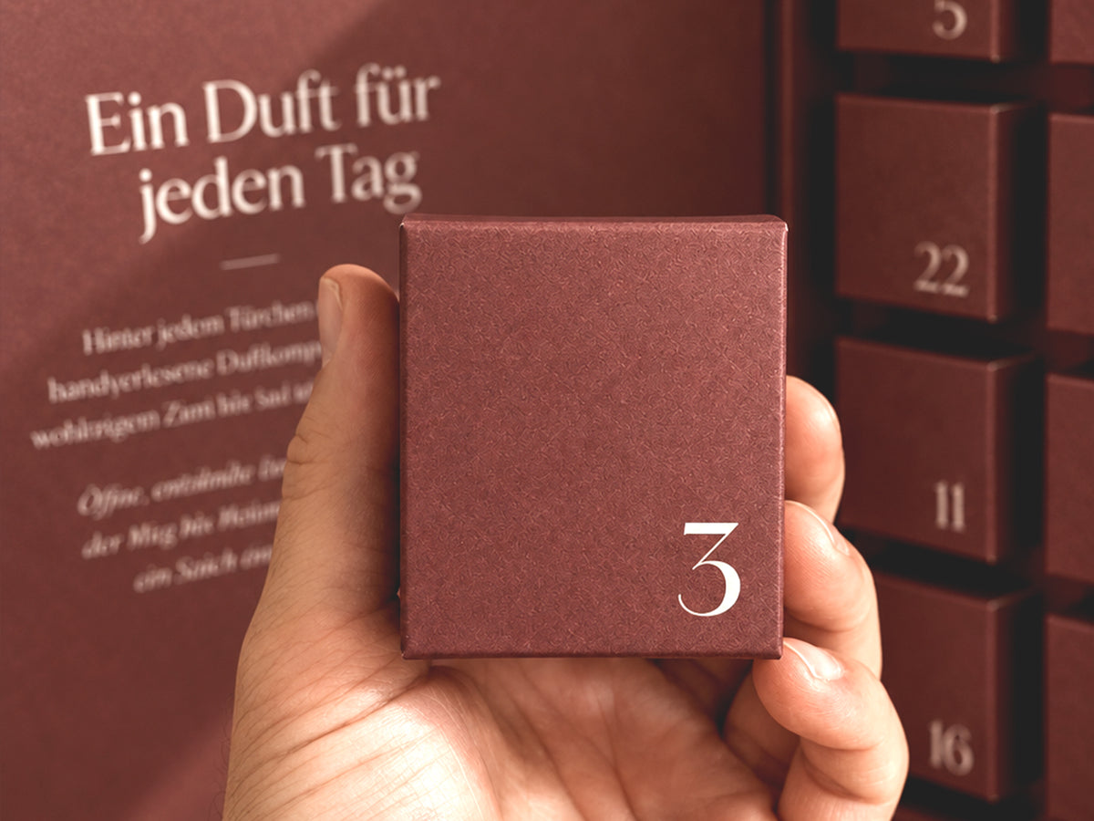 Hand hält die beerenrote Schachtel Nummer 3 vor dem geöffneten Adventskalender