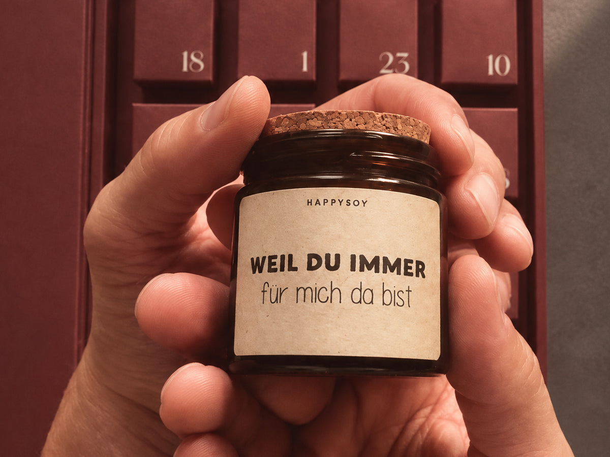 Hand hält eine HAPPYSOY Duftkerze mit der Botschaft Weil du immer für mich da bist